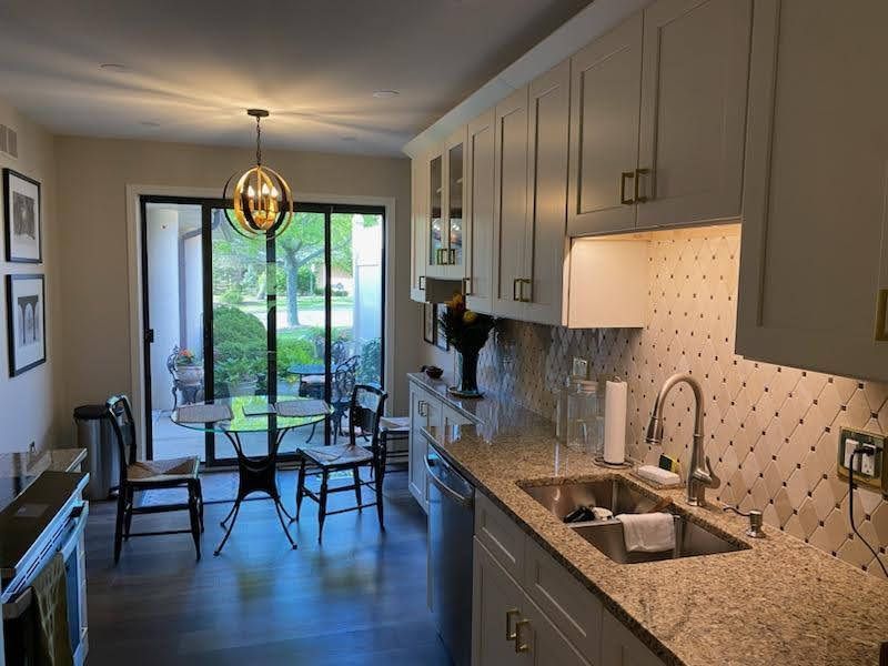 Modern kitchen with granite counters, sink, cabinets, and a small dining area by sliding glass doors