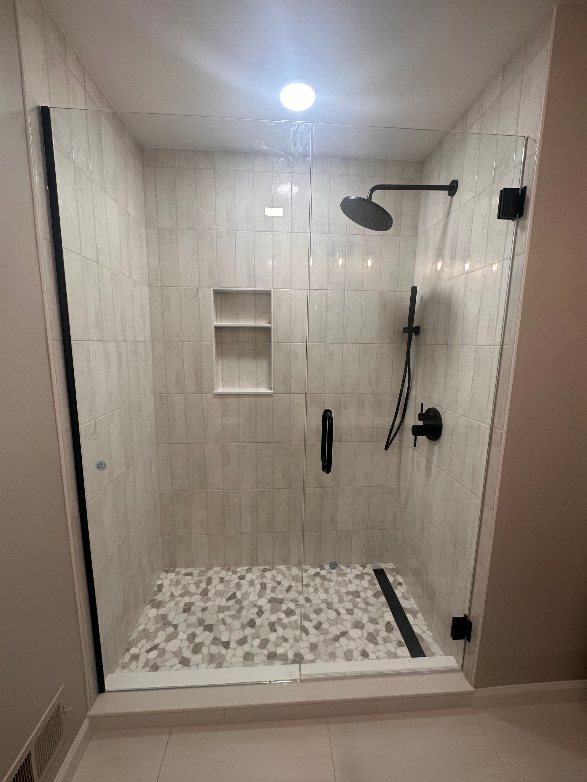 Walk-in shower with beige tile, pebble floor, built-in niches, grab bar, and rain showerhead.
