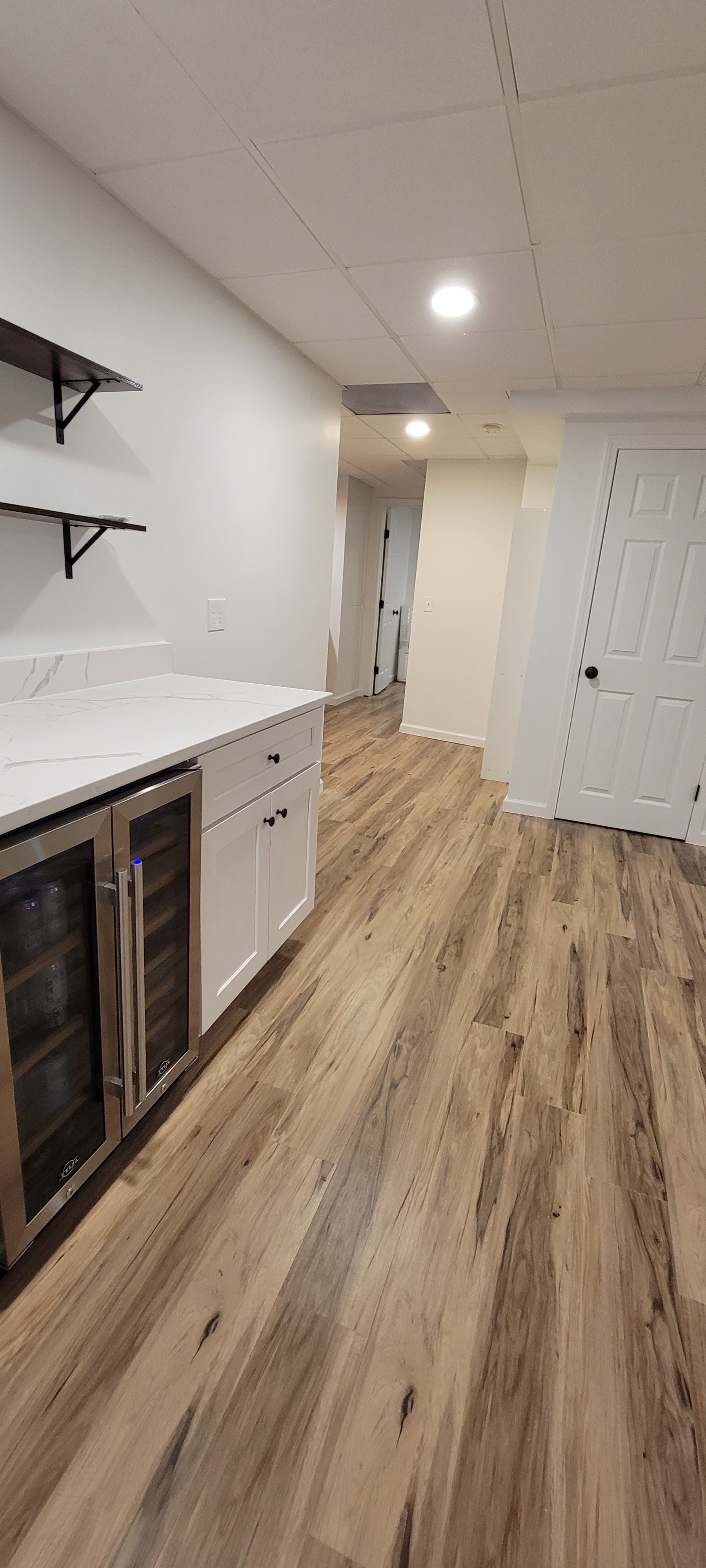Narrow modern kitchen hallway with white cabinets, wood floors, and a door at the end.