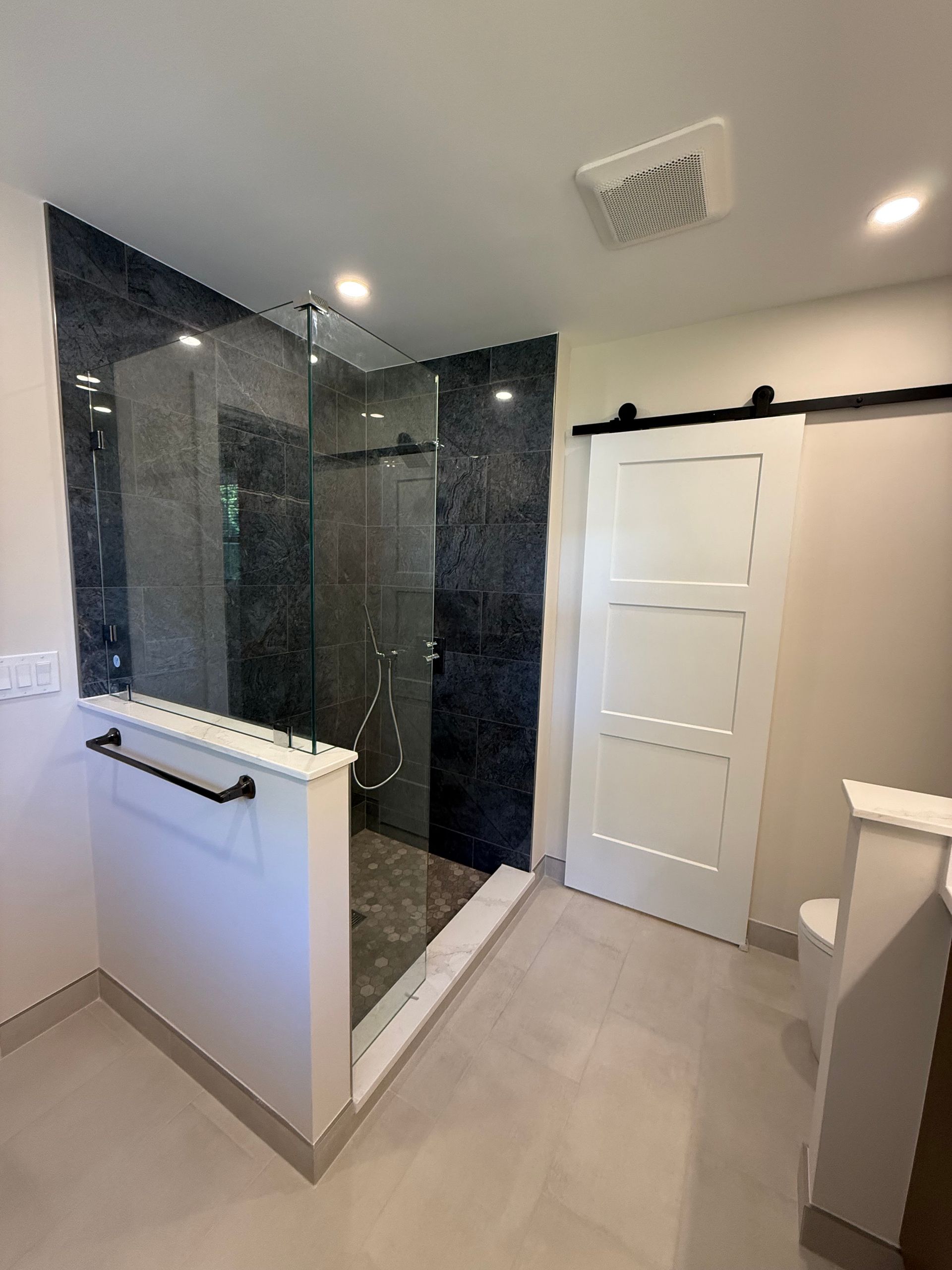 Modern bathroom with dark tiled shower, glass partition, white door, and beige floor tiles