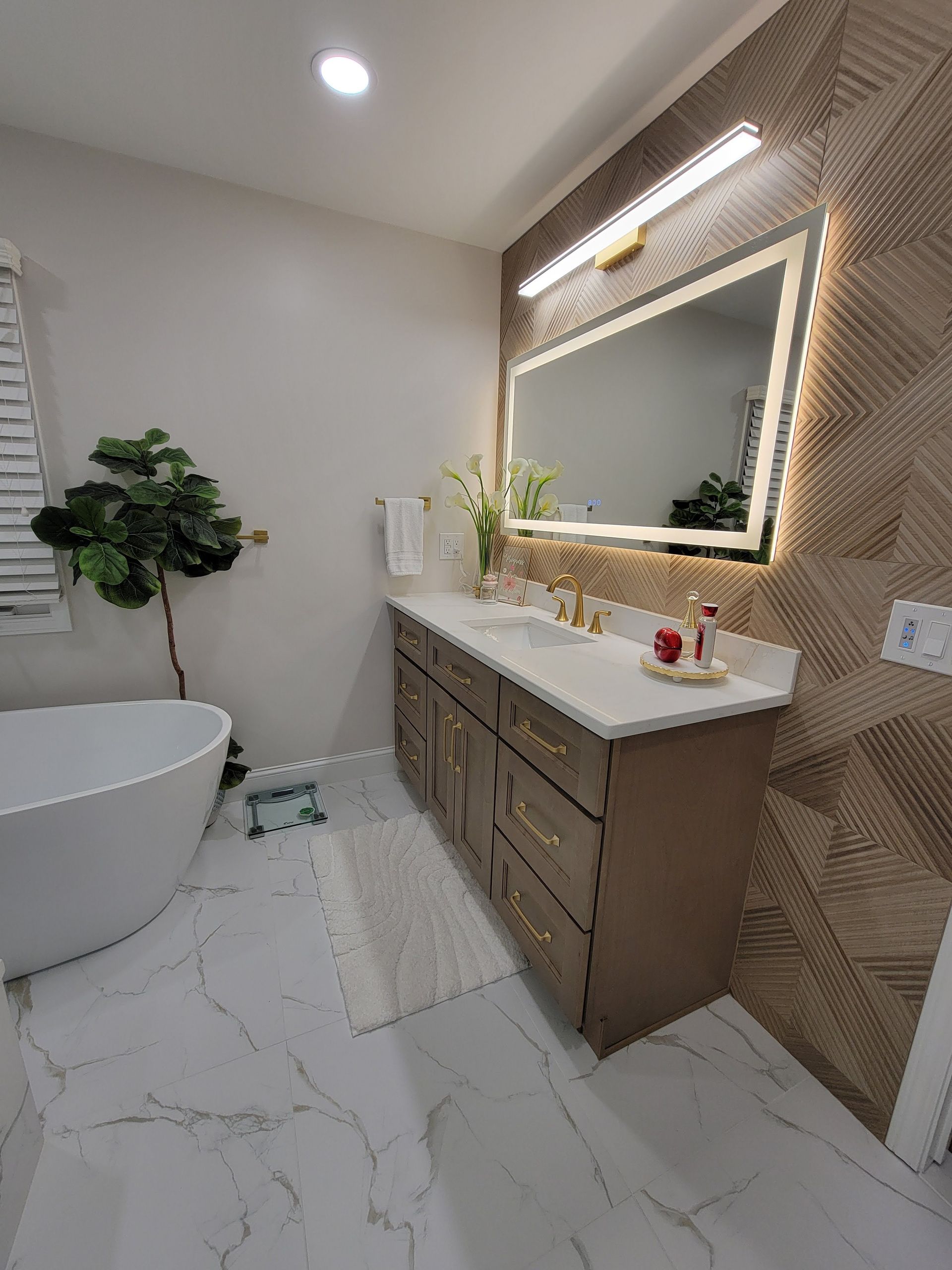 Modern bathroom with freestanding tub, marble vanity, lit mirror, and wood accent wall