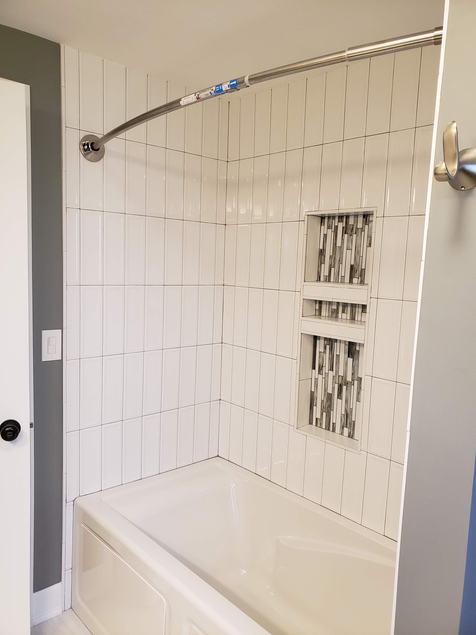 White bathroom tub and shower with a tiled wall, chrome shower curtain rod, and built-in soap niche