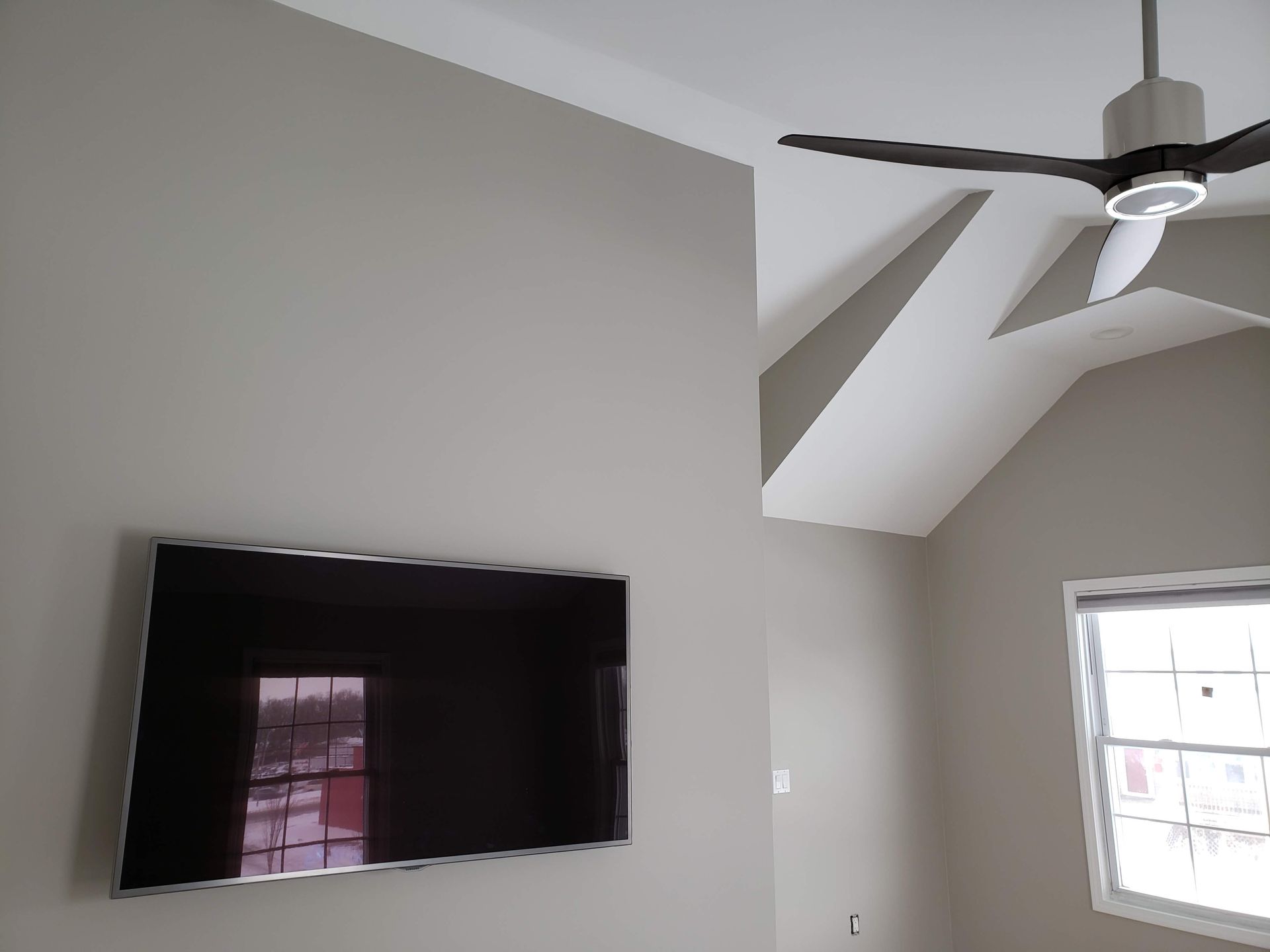 Living room with wall-mounted TV, high ceiling, ceiling fan, and bright window.