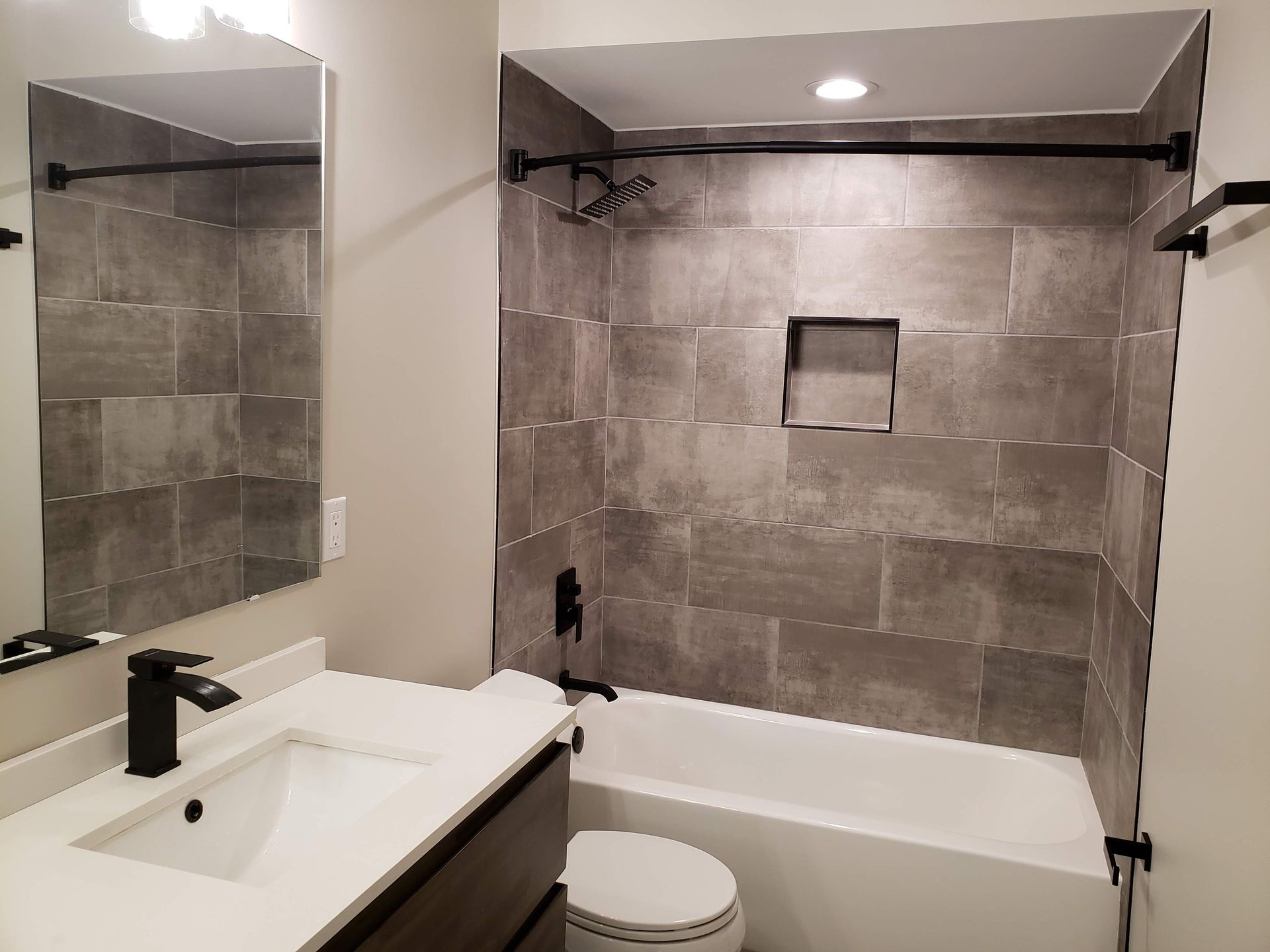 Modern bathroom with gray tile shower, white vanity, and toilet sink area