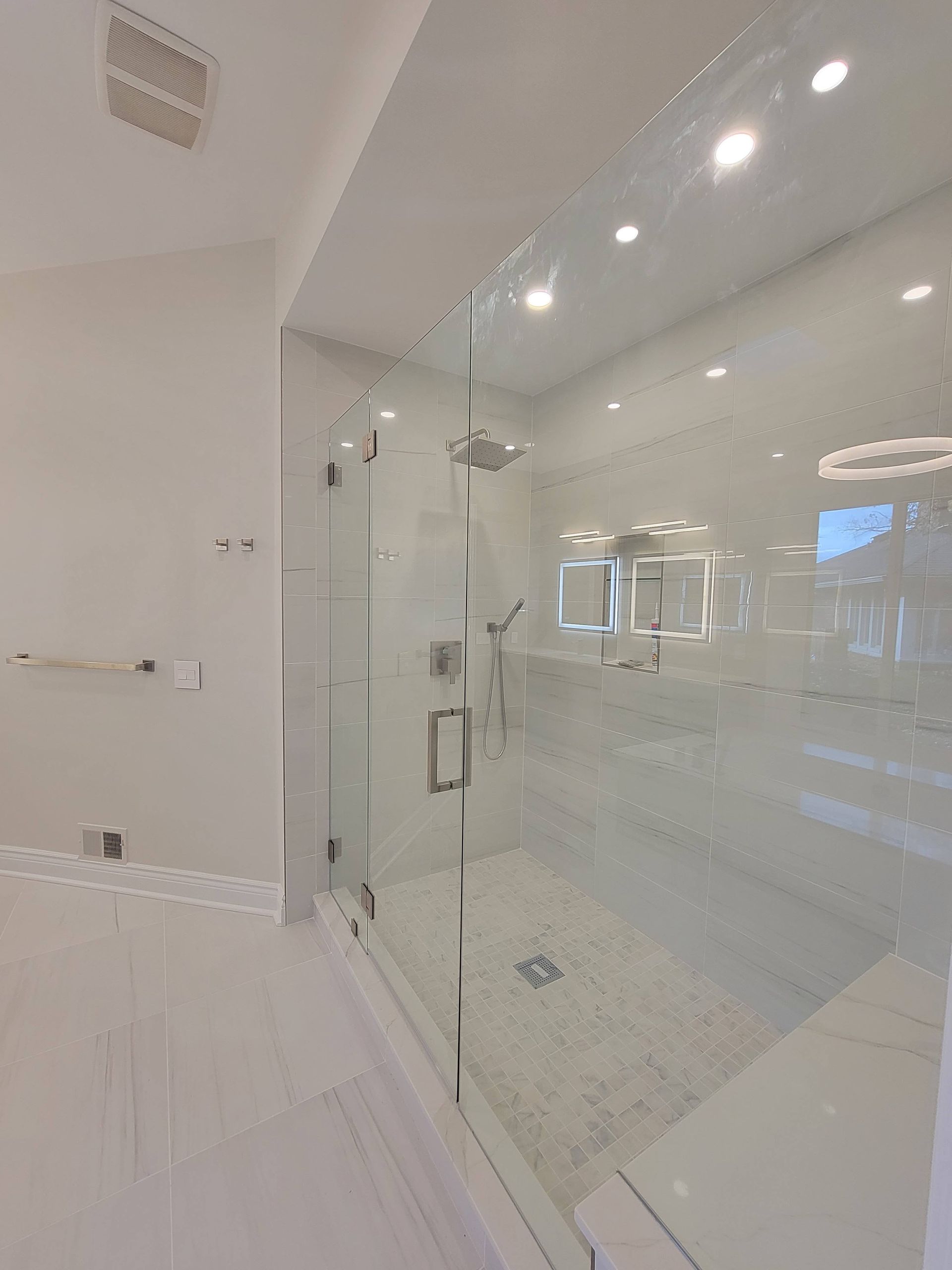 Modern white bathroom with glass shower enclosure, tiled floor, and recessed ceiling lights