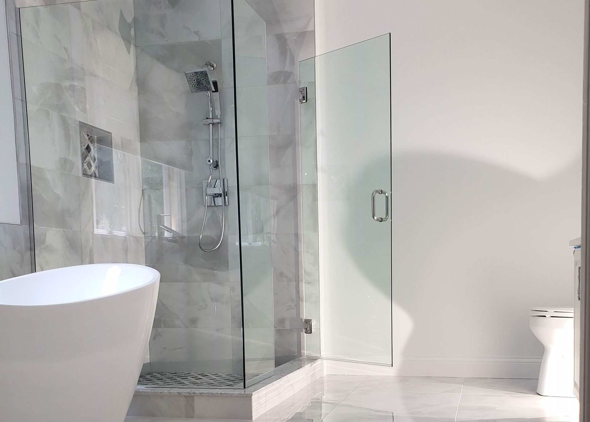 Modern bathroom with glass shower, white sink, and toilet on a marble floor