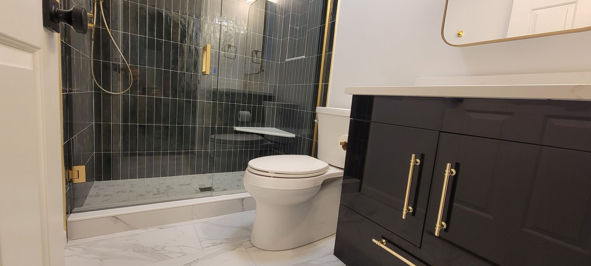 Modern bathroom with glass shower, white toilet, and black vanity with gold handles