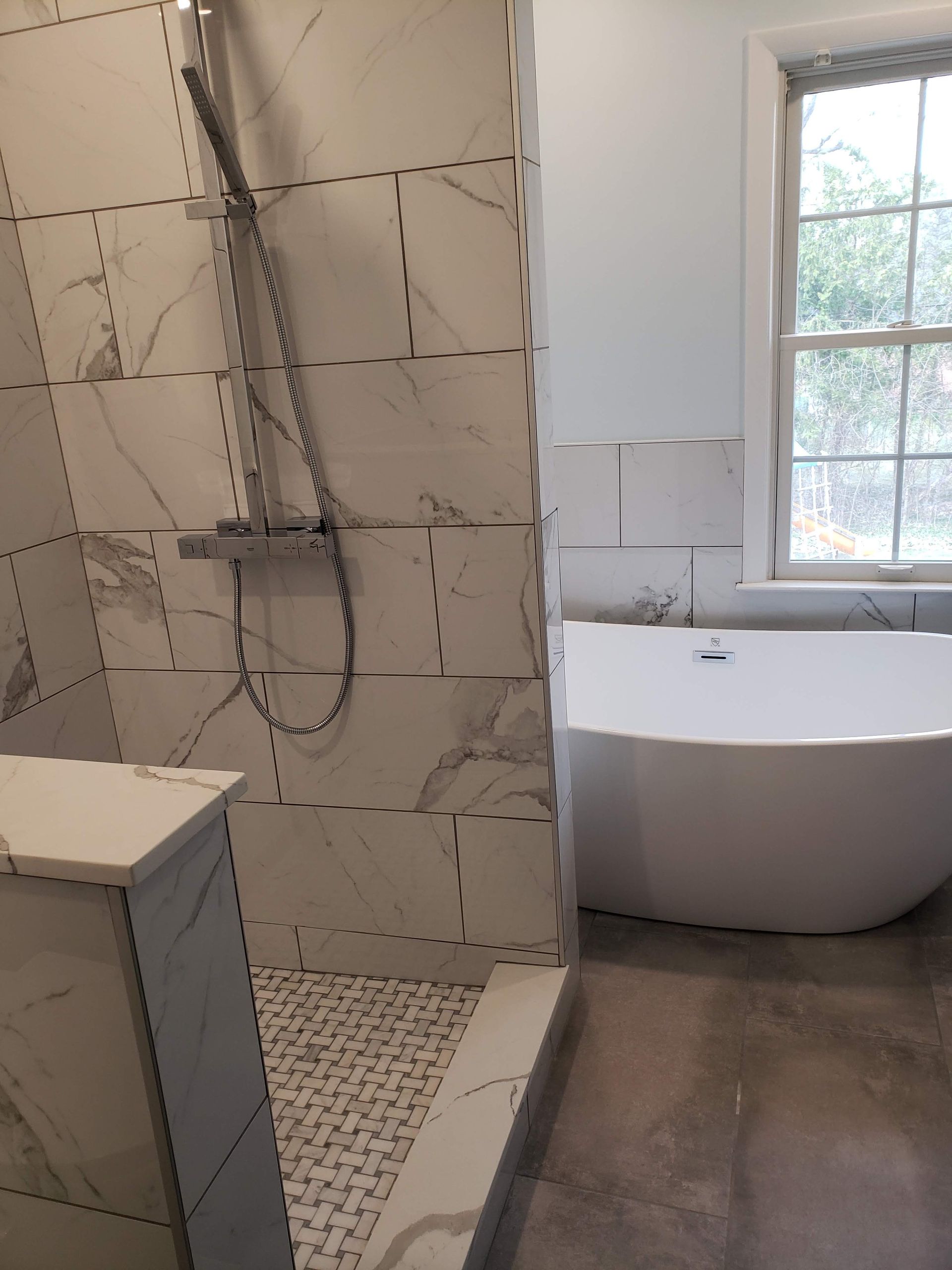 Modern bathroom with walk-in tiled shower, rainfall showerhead, and freestanding tub by a window.