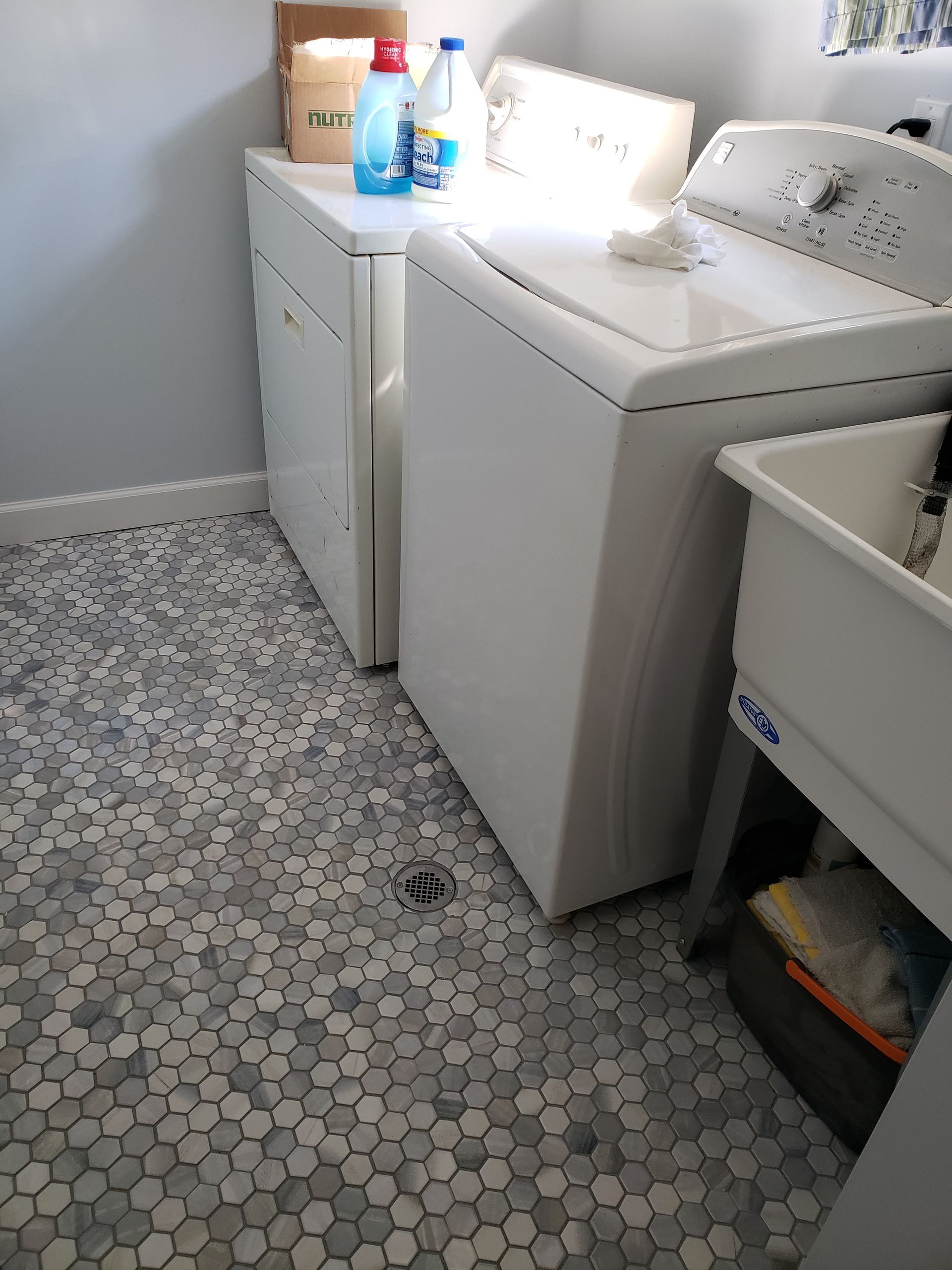 Laundry room with washer and dryer beside a sink, cleaner bottles on top, and a hex tile floor.
