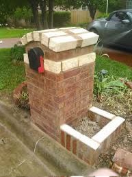 Brick mailbox beside a curb with a red flag raised, in a grassy yard near a parked car.
