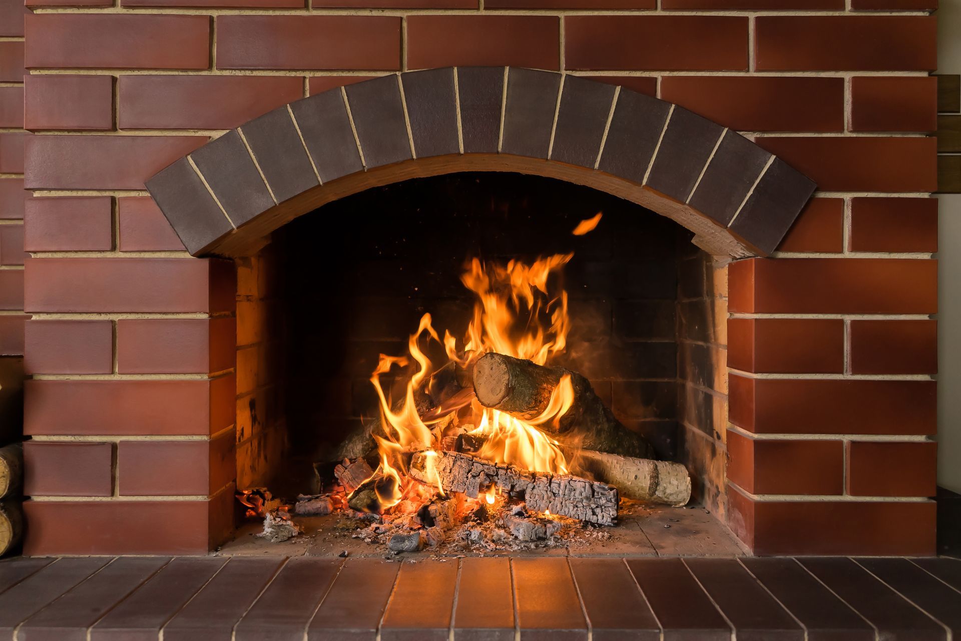 A roaring fire burns in an arched brick fireplace with a dark, tiled hearth.