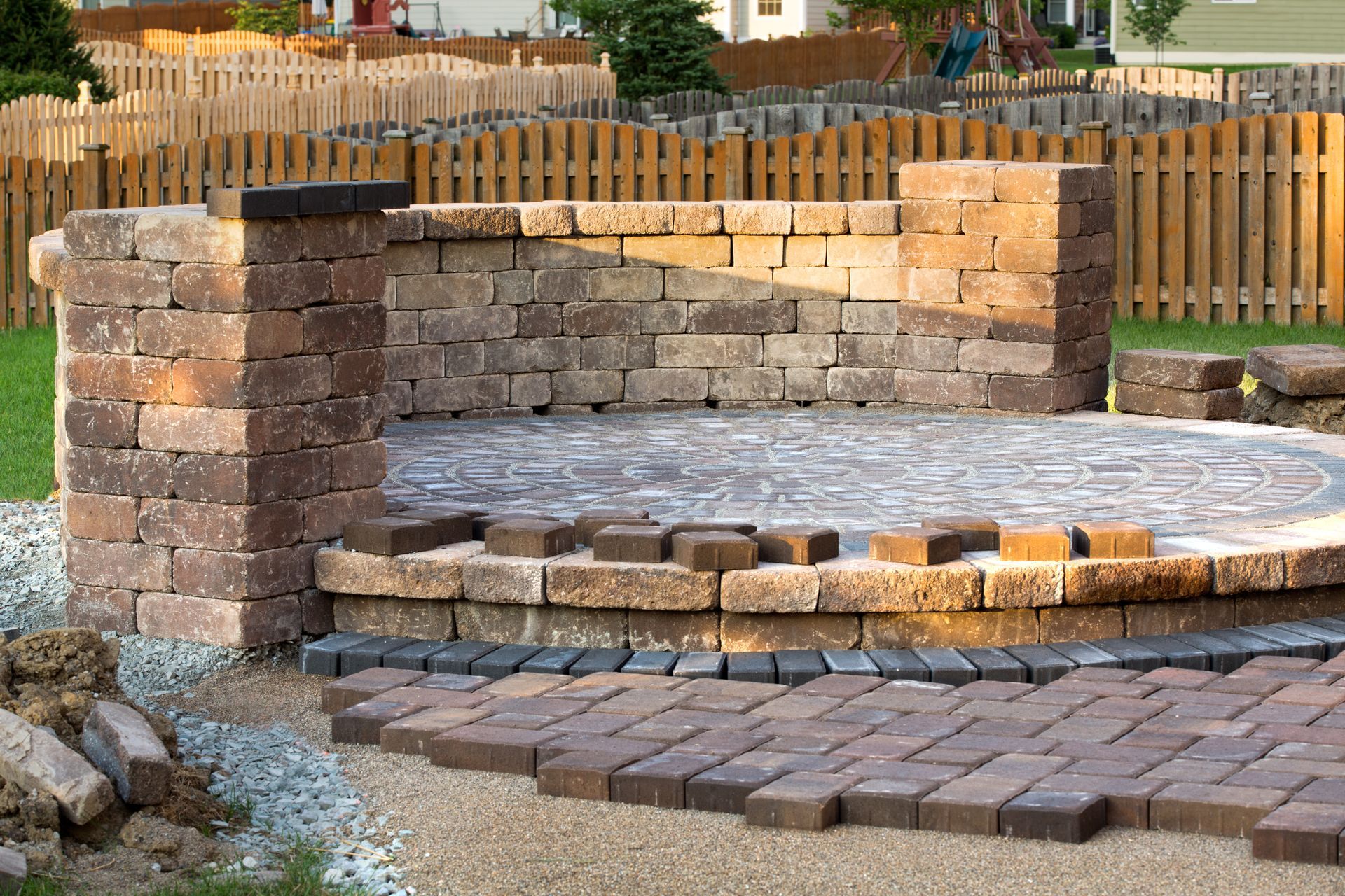 A partial construction site showing a circular stone patio with a curved brick retaining wall and unfinished brick pavers.