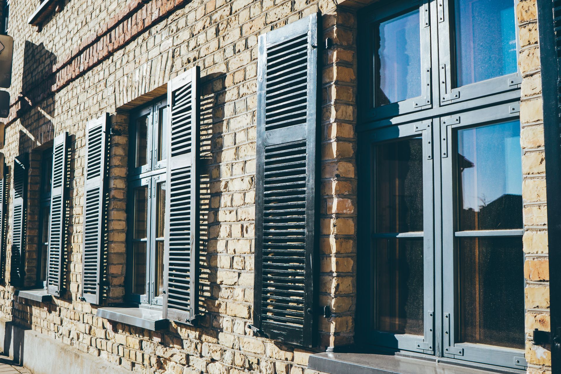 The exterior of a tan brick building featuring multiple dark-framed windows with black shutters.