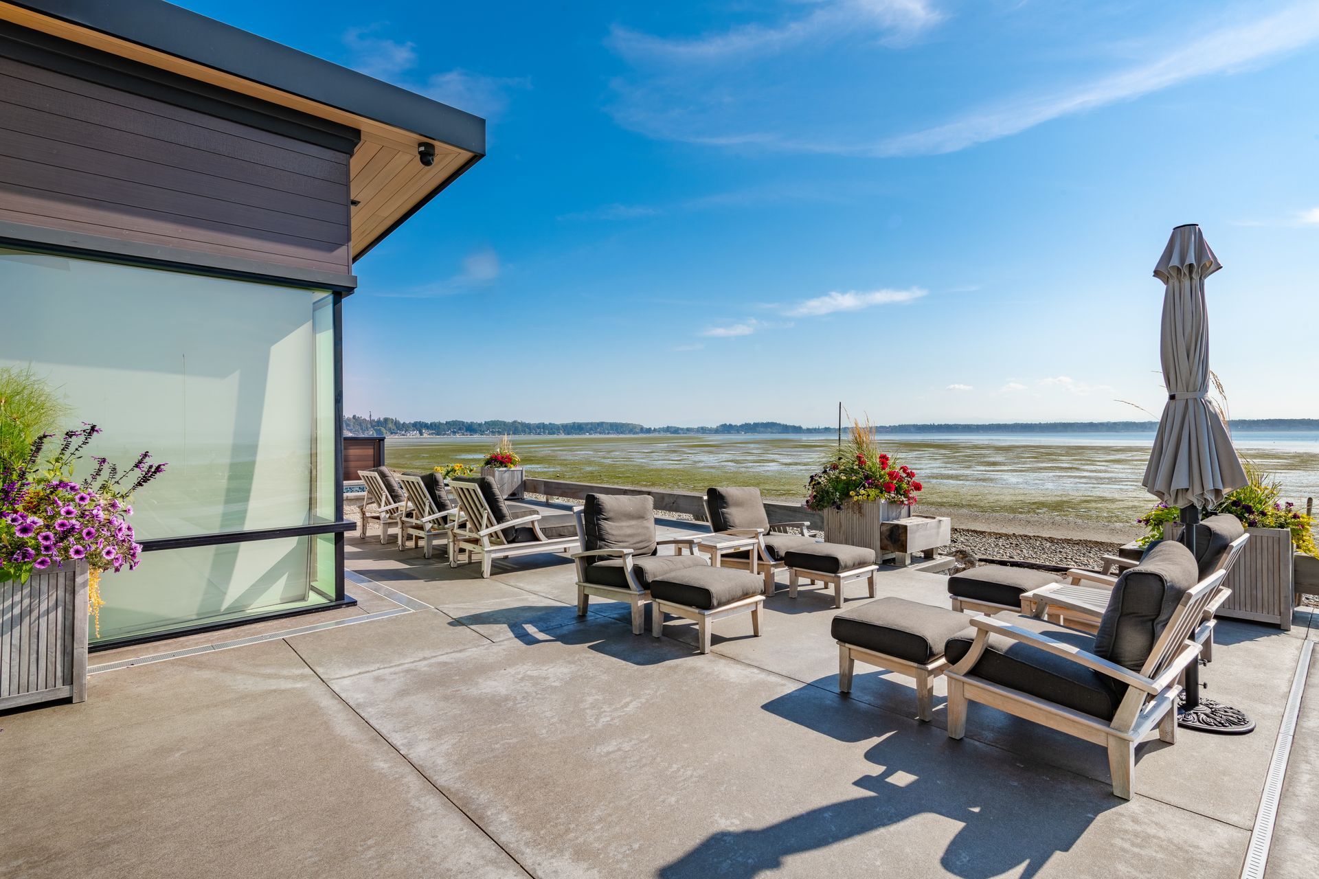 A sunny patio with outdoor furniture overlooking a coastal landscape with a calm bay and distant shore.