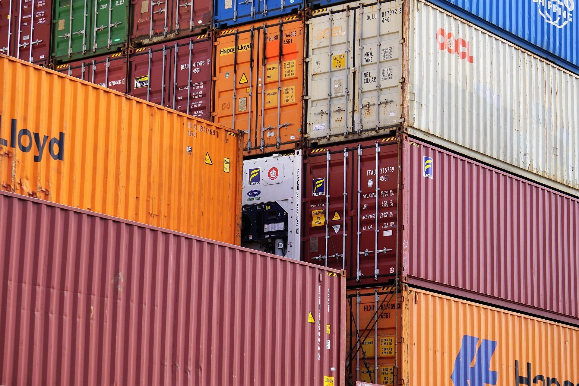 Contenedores de transporte apilados en colores naranja, rojo, azul y blanco en un depósito de carga.