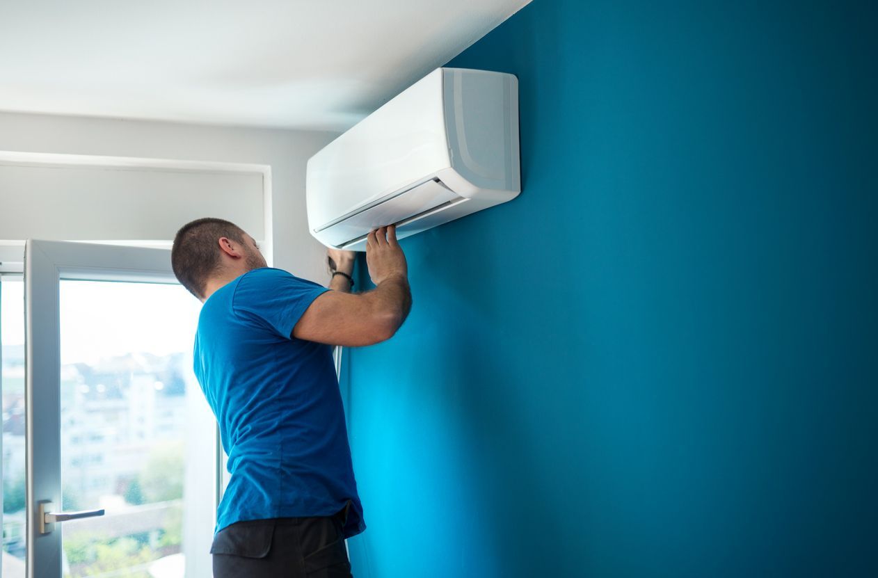 A man is installing an air conditioner on a blue wall.
