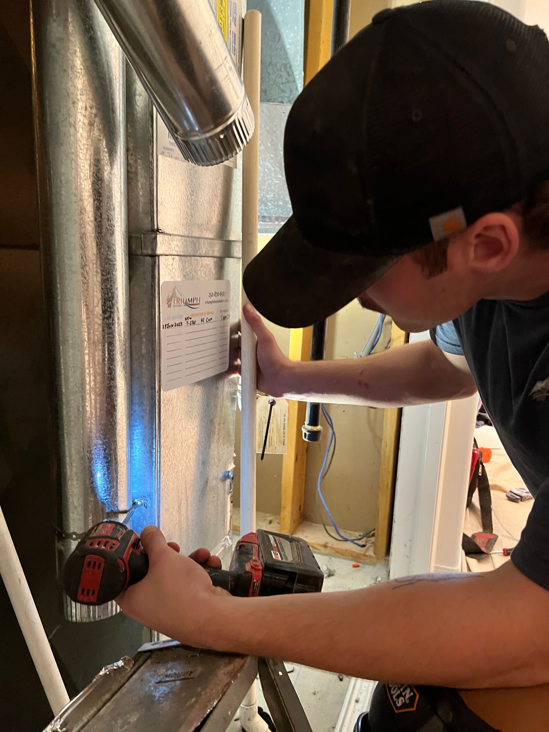 A man in a black hat is working on a pipe with a drill.