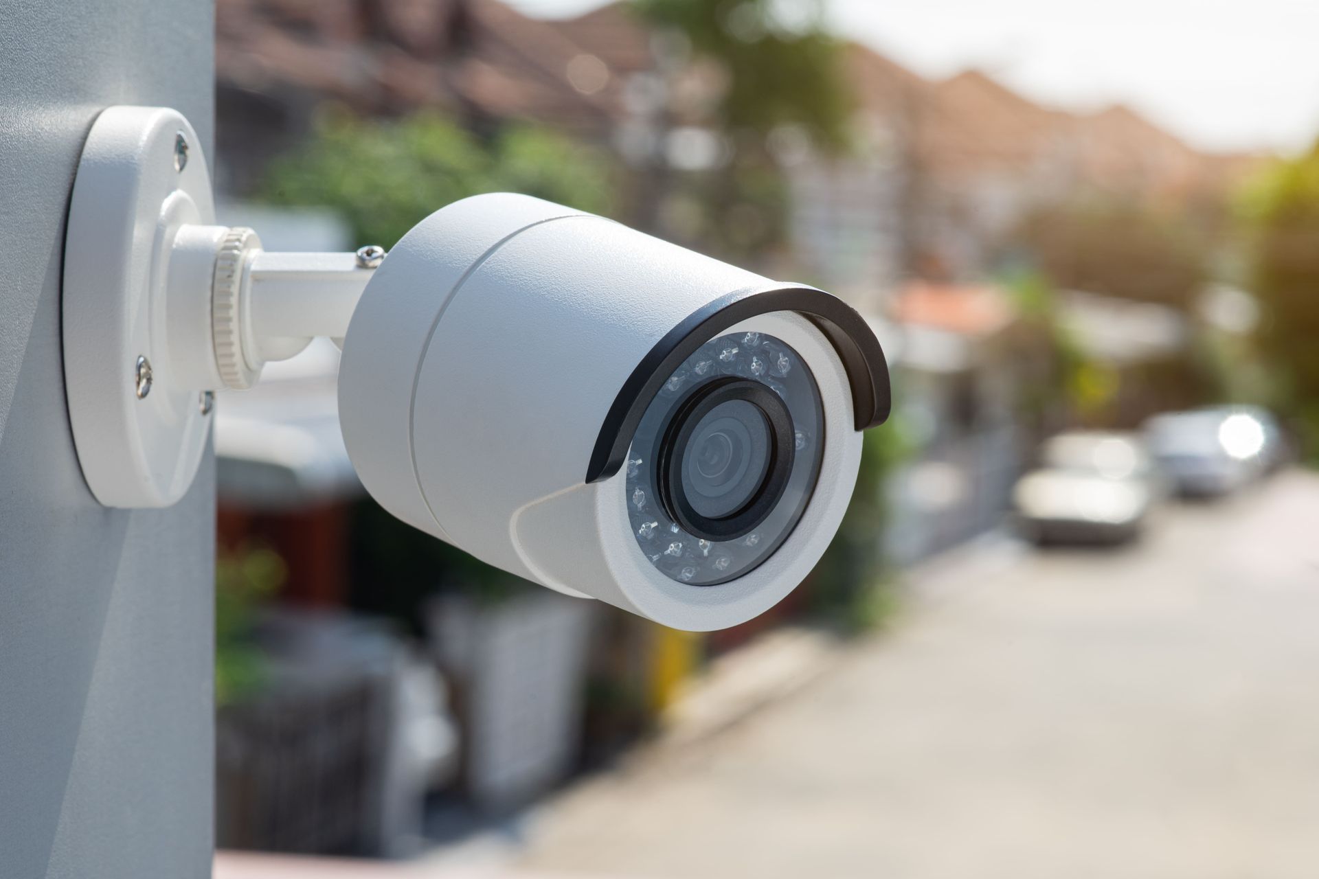 White outdoor security camera mounted on a pole, overlooking a residential street