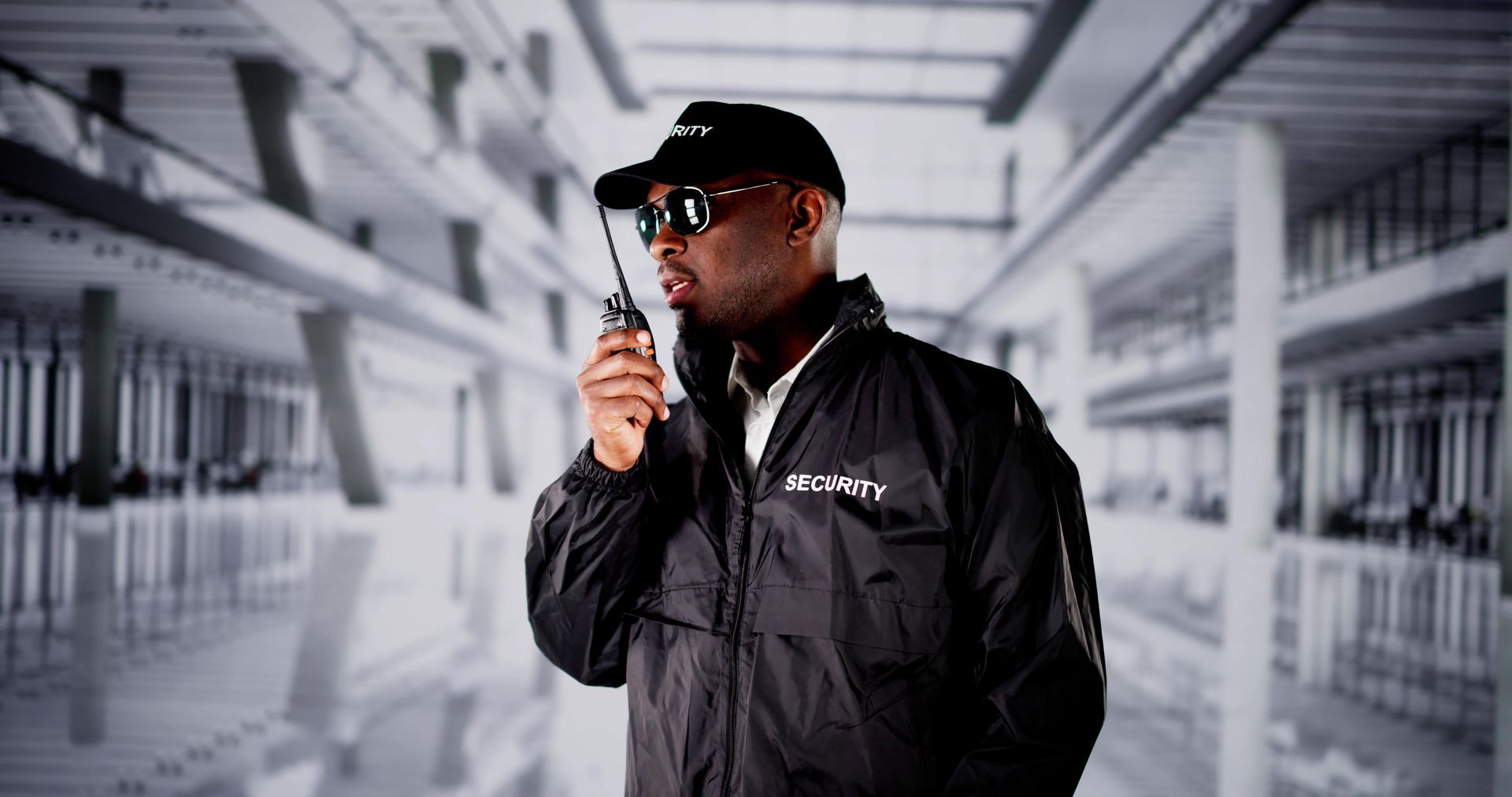 Security guard speaking into a walkie-talkie in a bright industrial hallway.