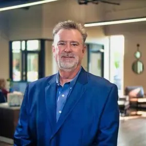 Man in a blue suit standing in a modern office lobby, looking at the camera.