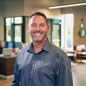 Smiling man in a gray shirt standing in a bright office lobby