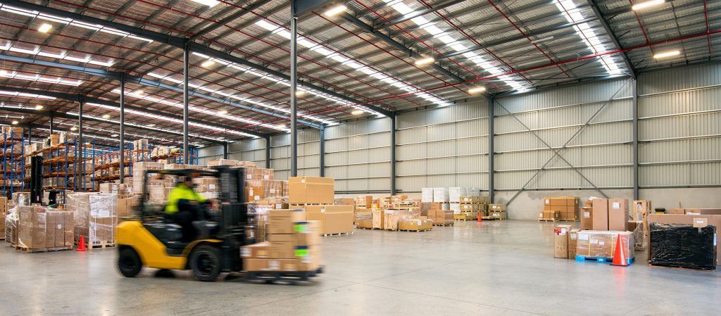 Forklift moving pallets in a large warehouse with stacked boxes and high shelving