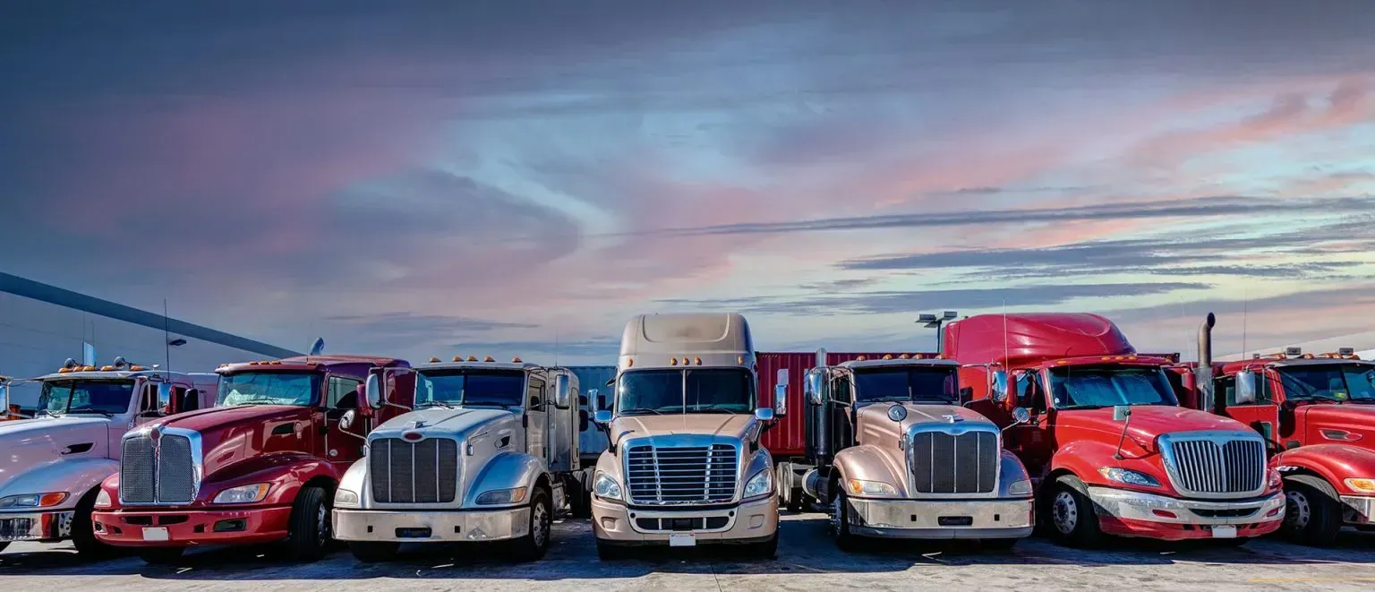 Line of colorful semi trucks parked side by side at dusk under a pastel sky