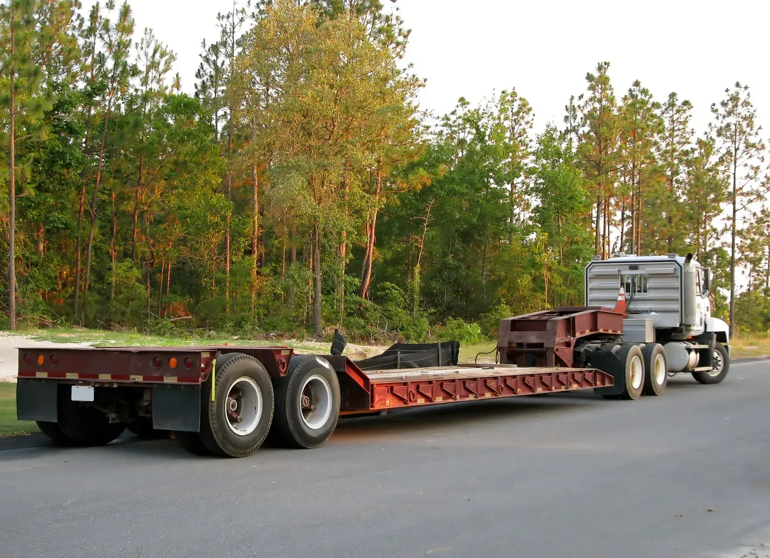 Semi-truck hauling a long red flatbed trailer on a road beside trees