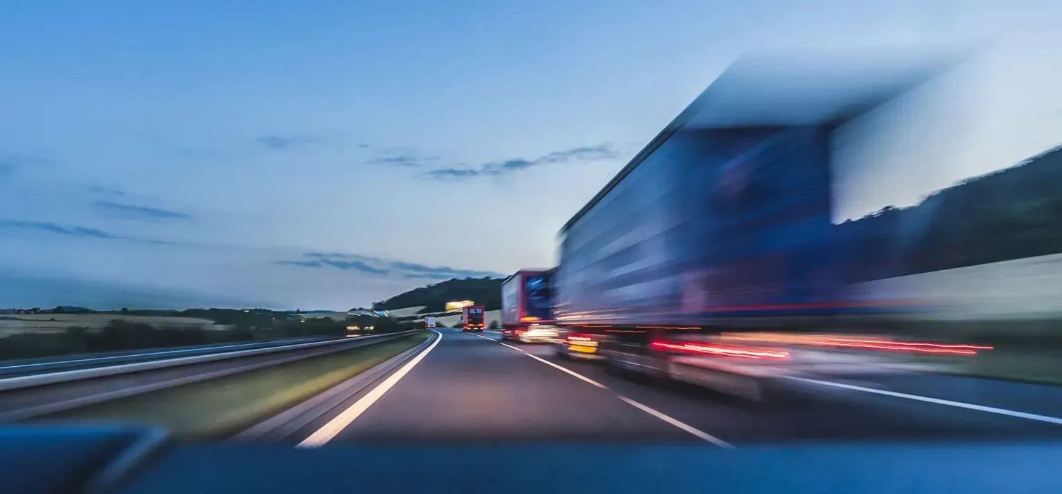Blurred cars speeding on a highway at dusk, with motion streaks and a blue truck on the right