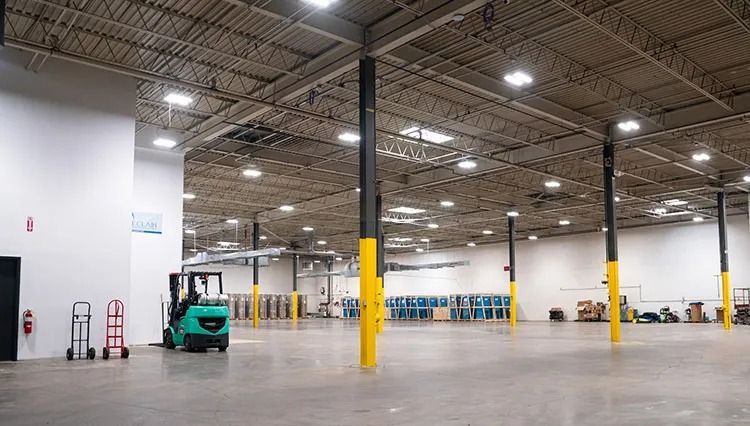 Empty warehouse with a small green forklift, concrete floor, and yellow support columns under bright lights