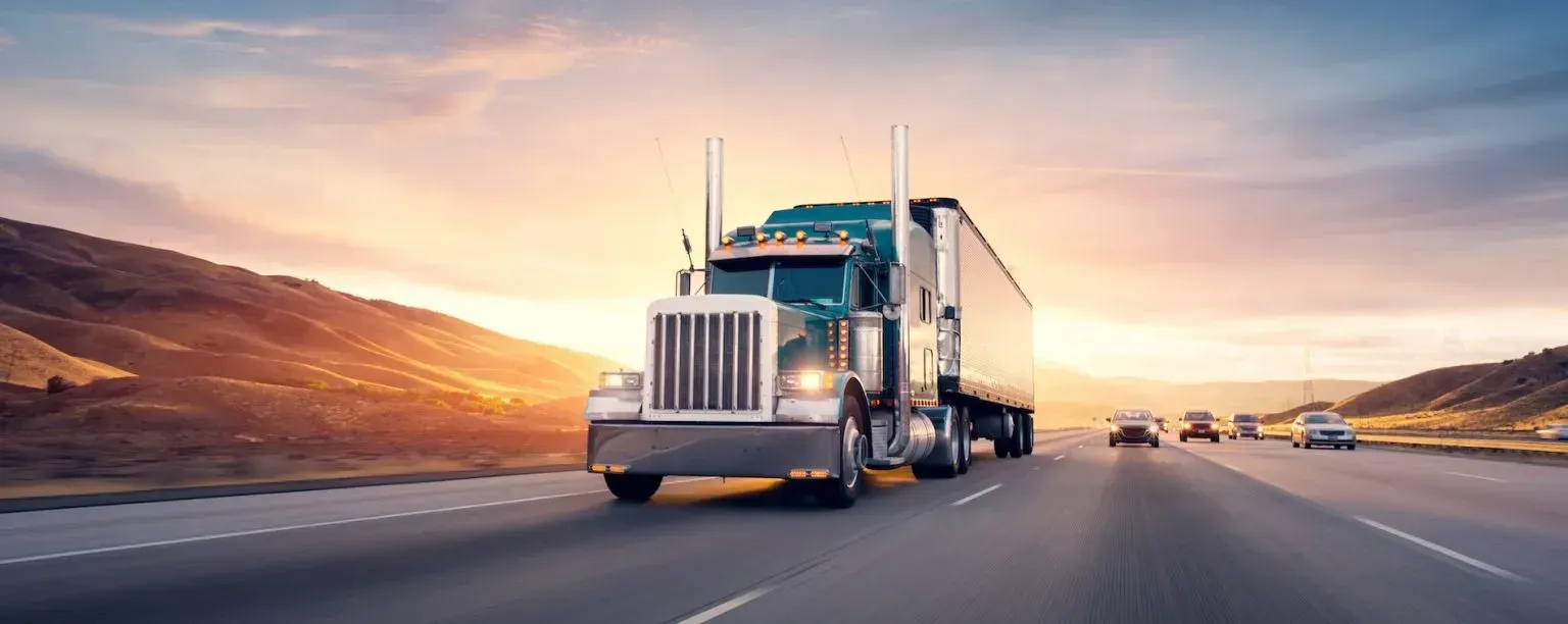 Semi truck driving on a highway at sunset with mountains in the background