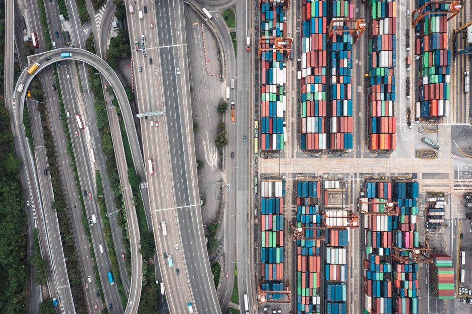 Aerial view of a highway interchange beside a dense container port with stacked colorful shipping containers