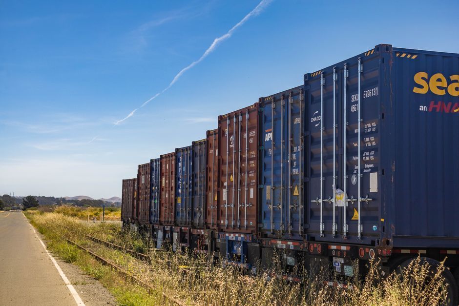 Long freight train of shipping containers beside a rural road under a blue sky
