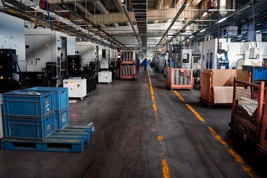 Industrial warehouse aisle with machinery, pallets, and blue bins along a marked concrete floor