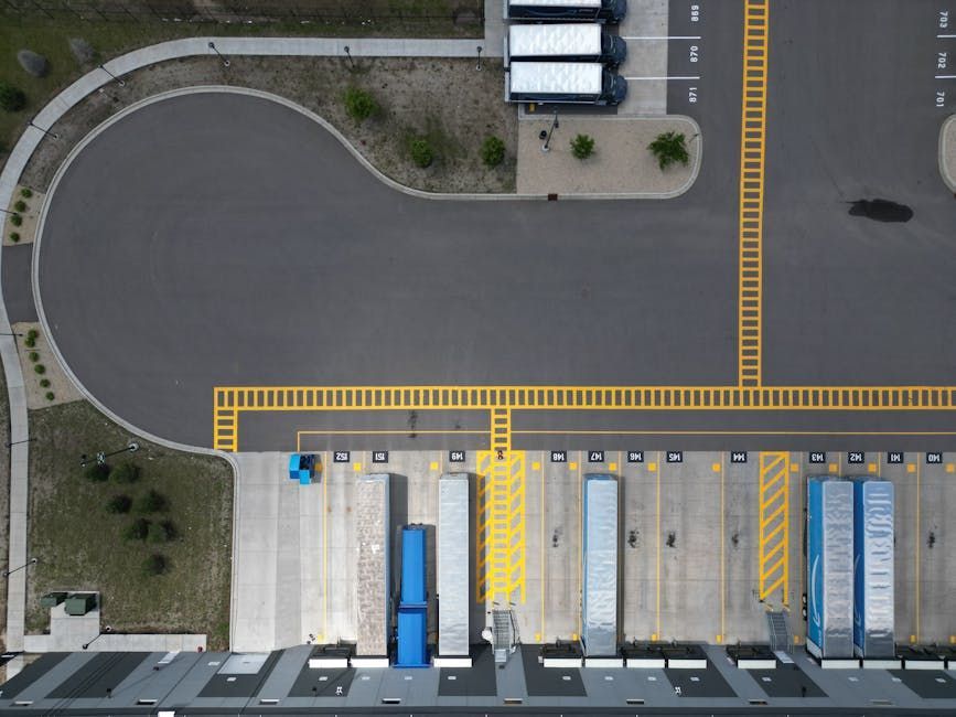 Aerial view of a truck loading dock with parked trailers, yellow lane markings, and a curved roadway.