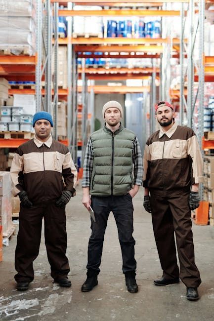 Three warehouse workers standing in an aisle between tall shelving racks