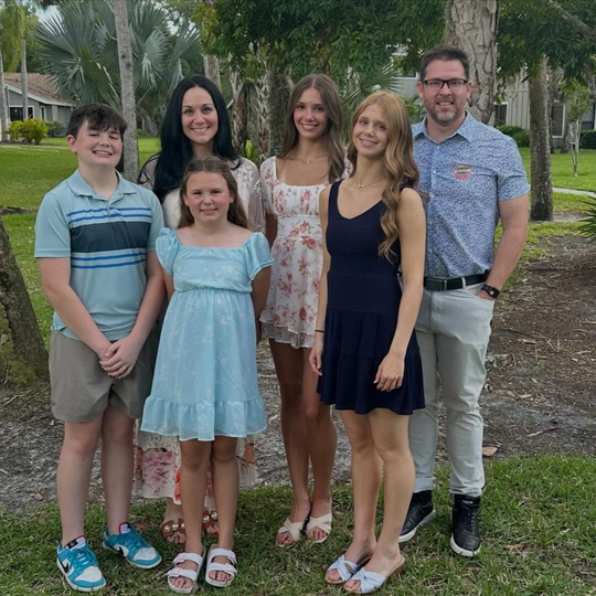 Christian Medford with his family outdoors in a park with palm trees and greenery.