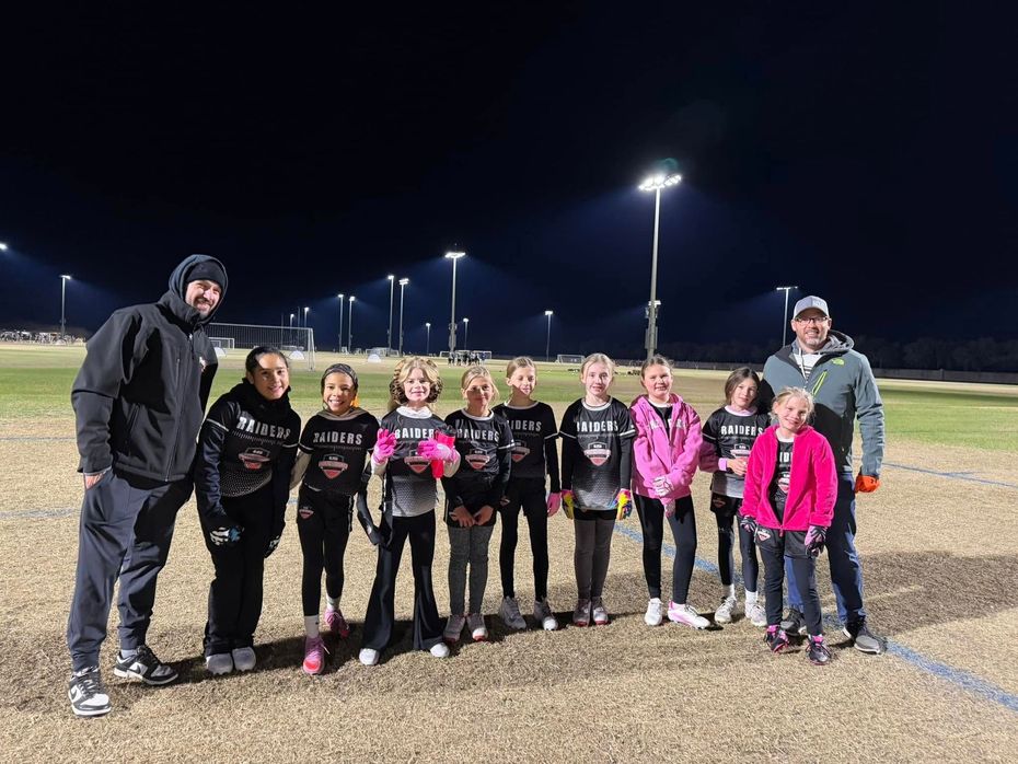 Christian Medford and youth soccer team posing on a lit field at night, wearing black and pink uniforms with two coaches.