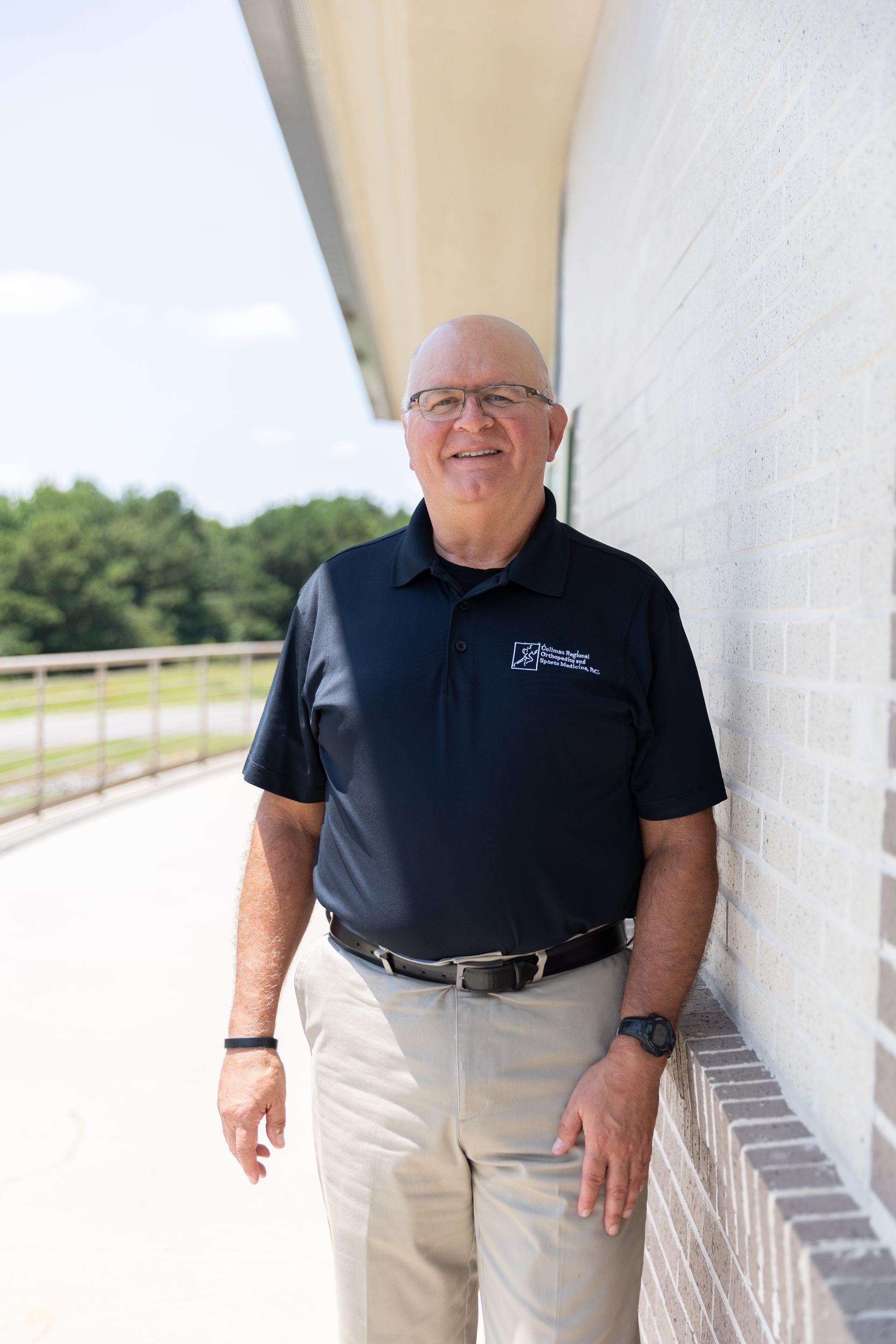 Dr. Ben Gomez in a blue shirt is standing with his arms crossed and smiling.
