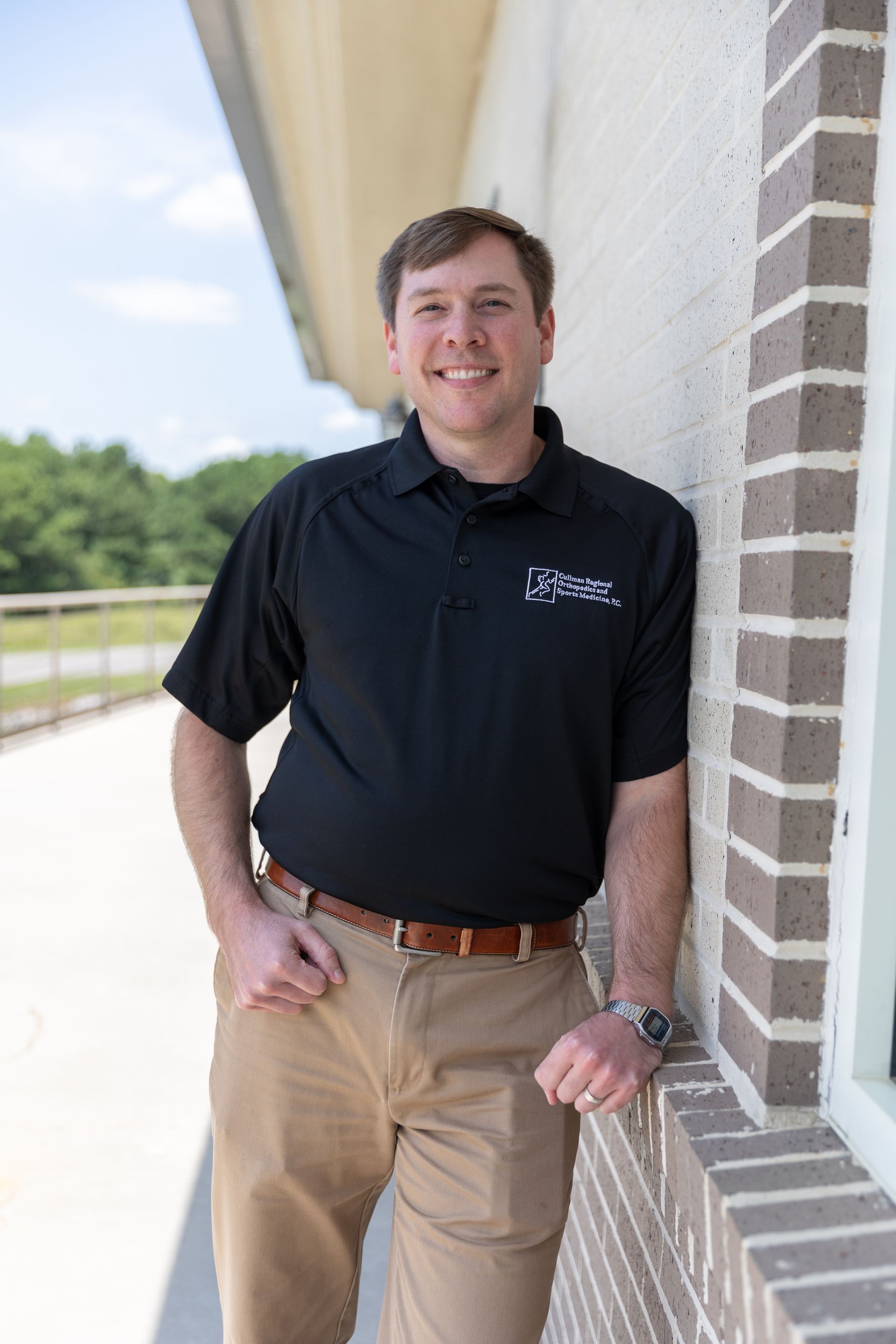 Patrick Harbison, CRNP in a black shirt and khaki pants is standing next to a railing.