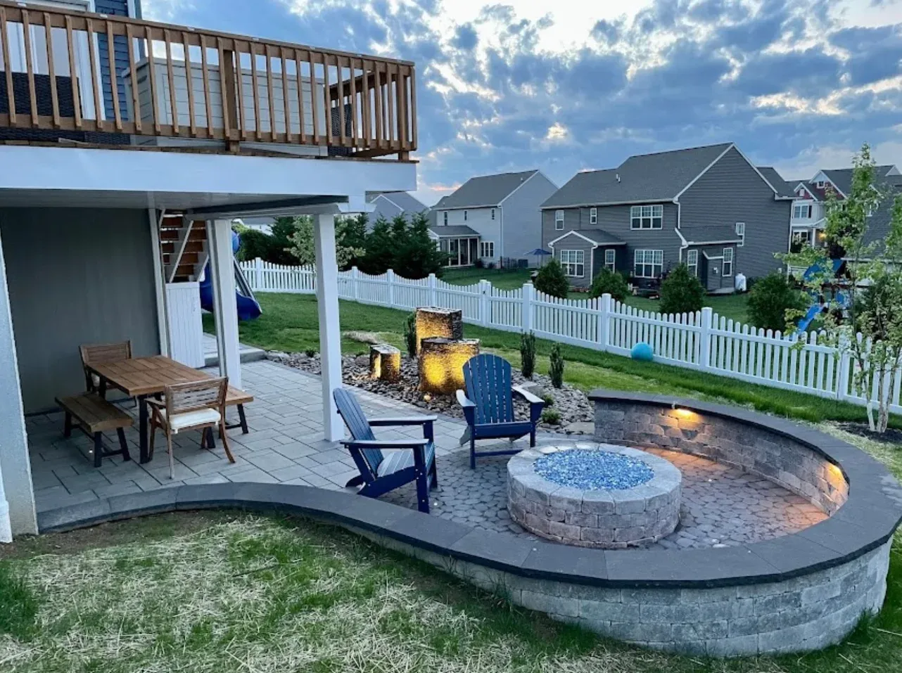 White vinyl fence with a gate, leading to a paved patio area. Dirt borders the walkway.