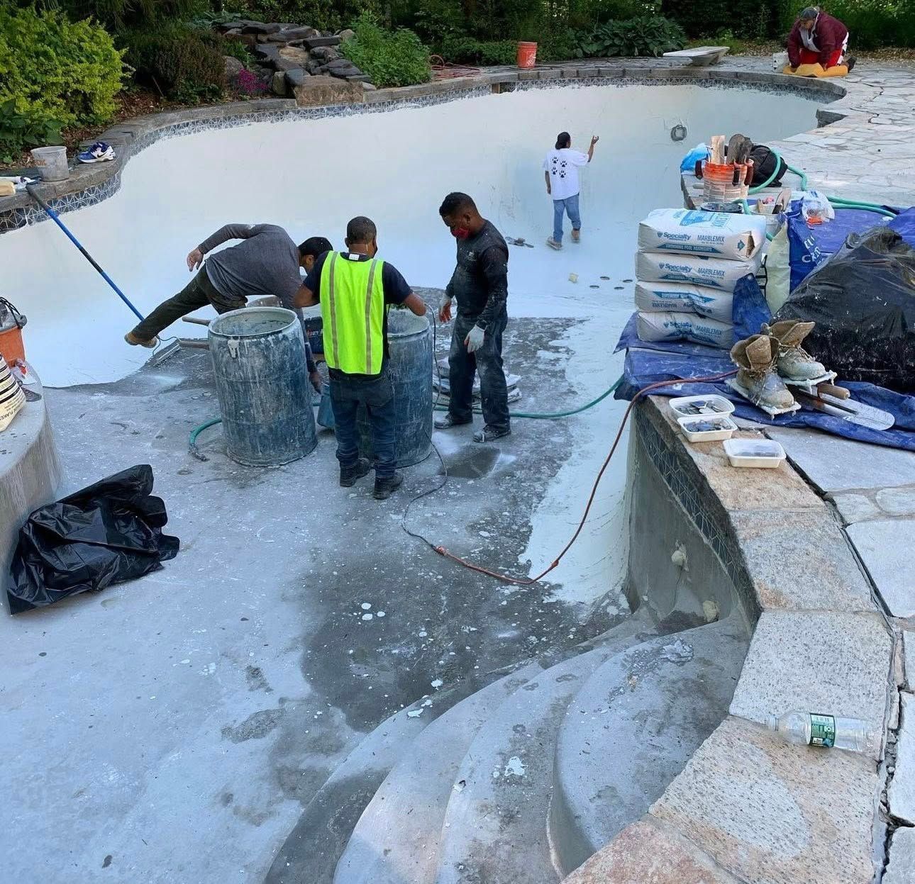 Pool construction: Workers inside a pool applying material. White walls, blue tile, stone steps.
