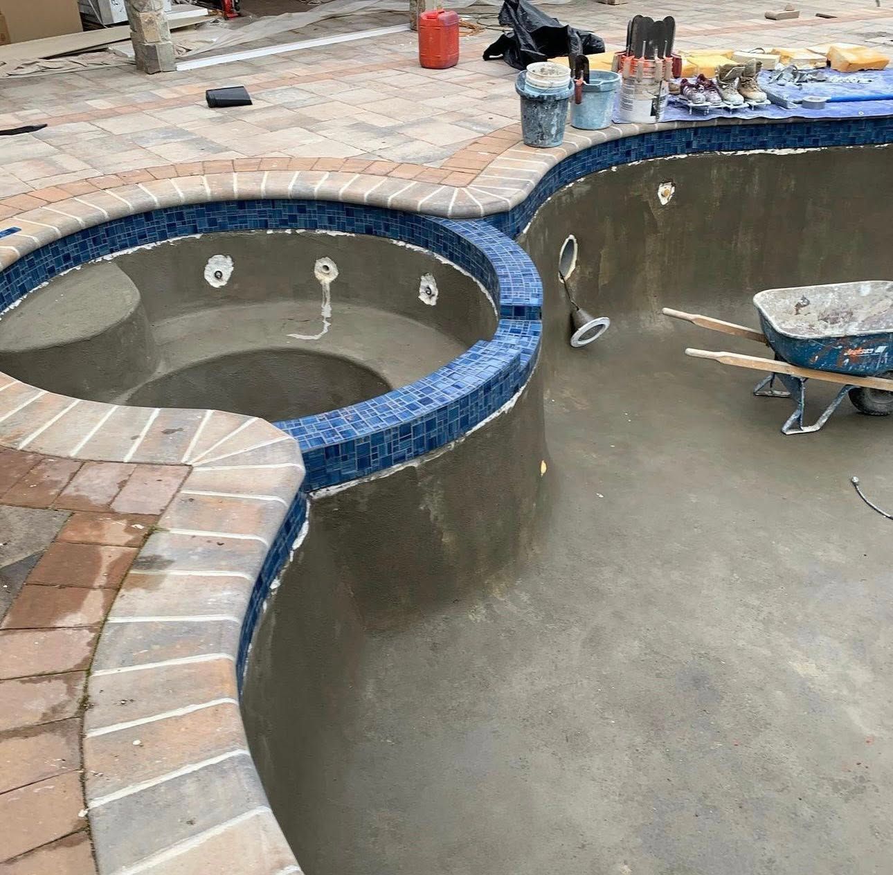 Pool and spa construction: empty basin, blue tile trim, brick edging, construction tools.