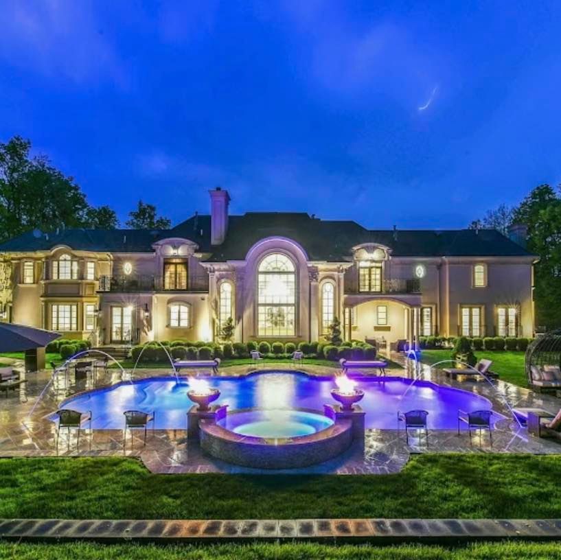Luxury mansion at dusk with illuminated pool and spa.