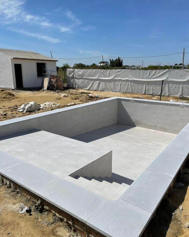 A partially constructed swimming pool with steps, next to a small white building, outdoors.