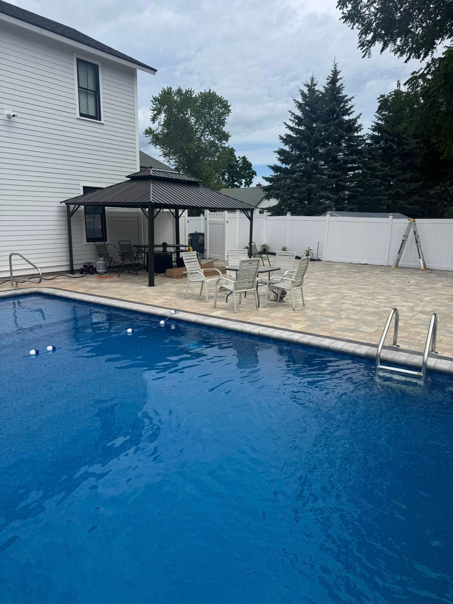 A pool with blue water, patio, and pergola beside a white house.