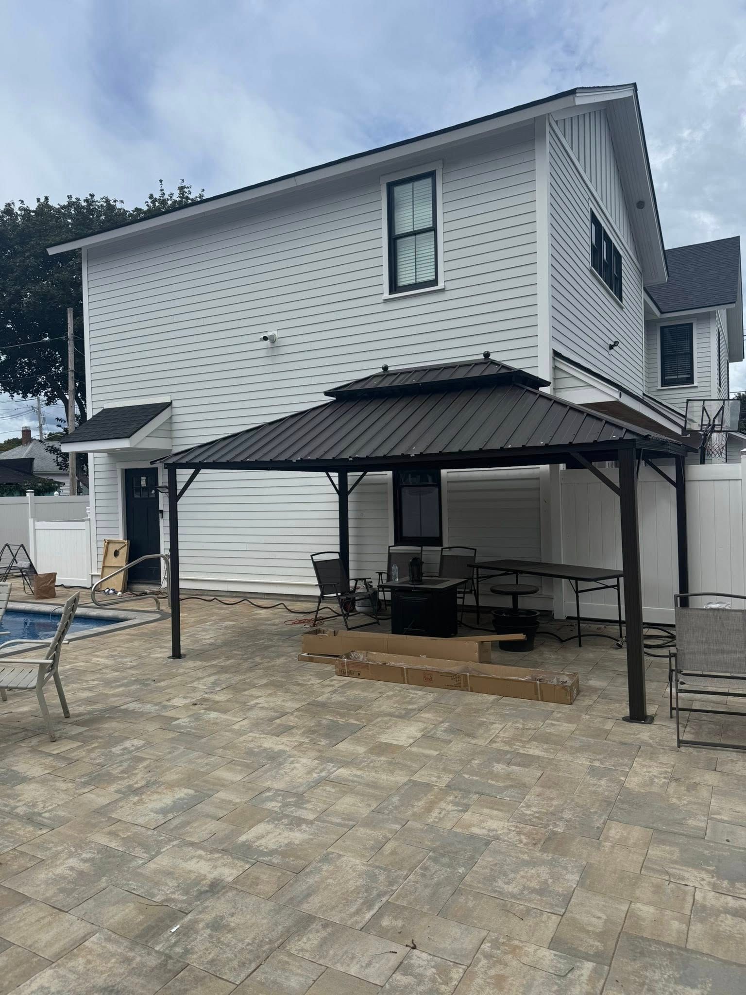 Backyard with gazebo, brick patio, white house, and a swimming pool.