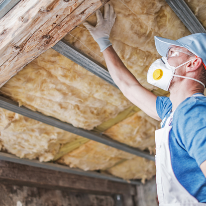 Man in protective gear installing insulation in a building's ceiling.