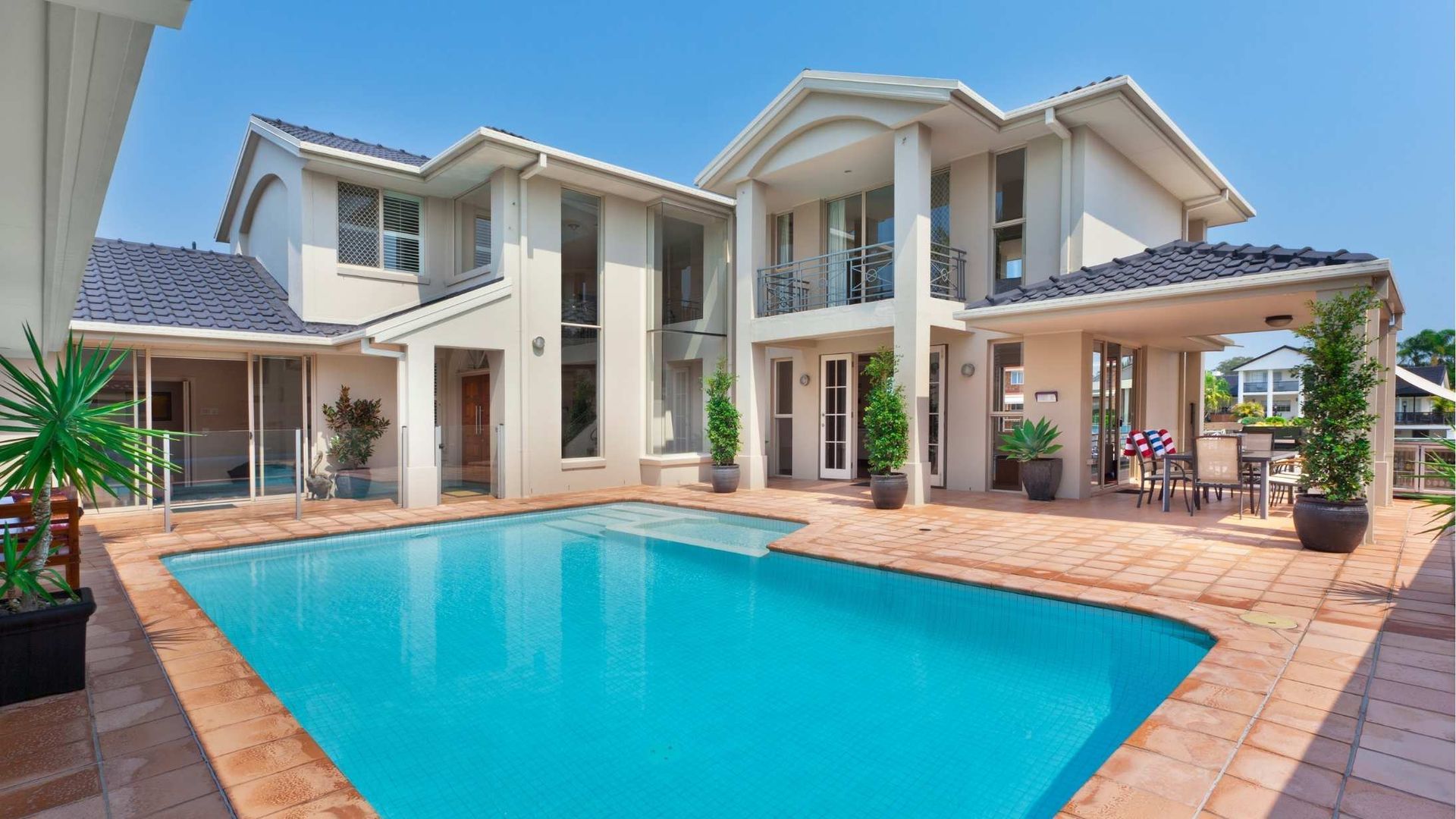 Large beige two-story house with a pool. The pool is turquoise, and there is a patio area with seating.