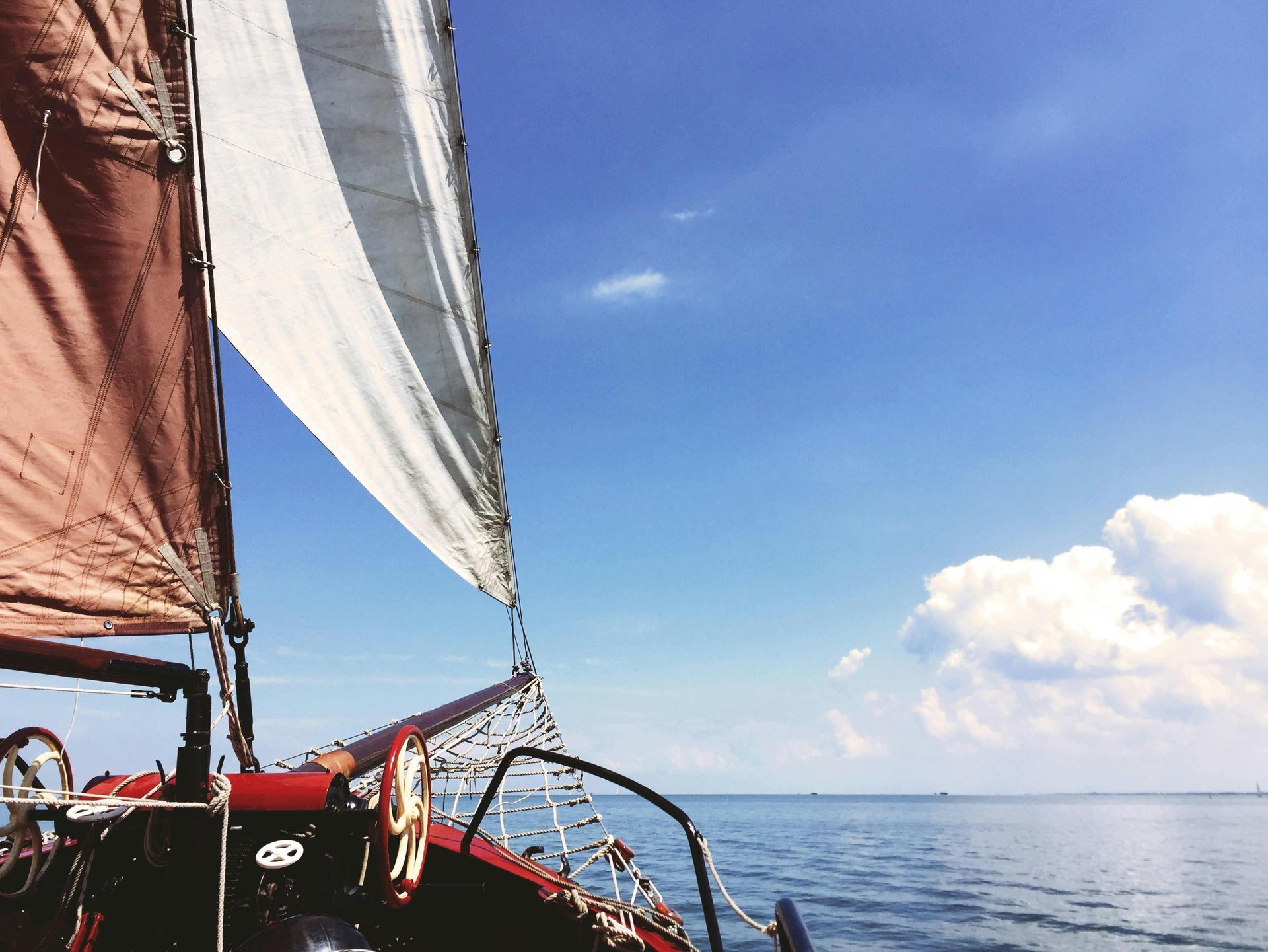 Sailboat at sea with sails filled by the wind, against a blue sky and fluffy clouds.